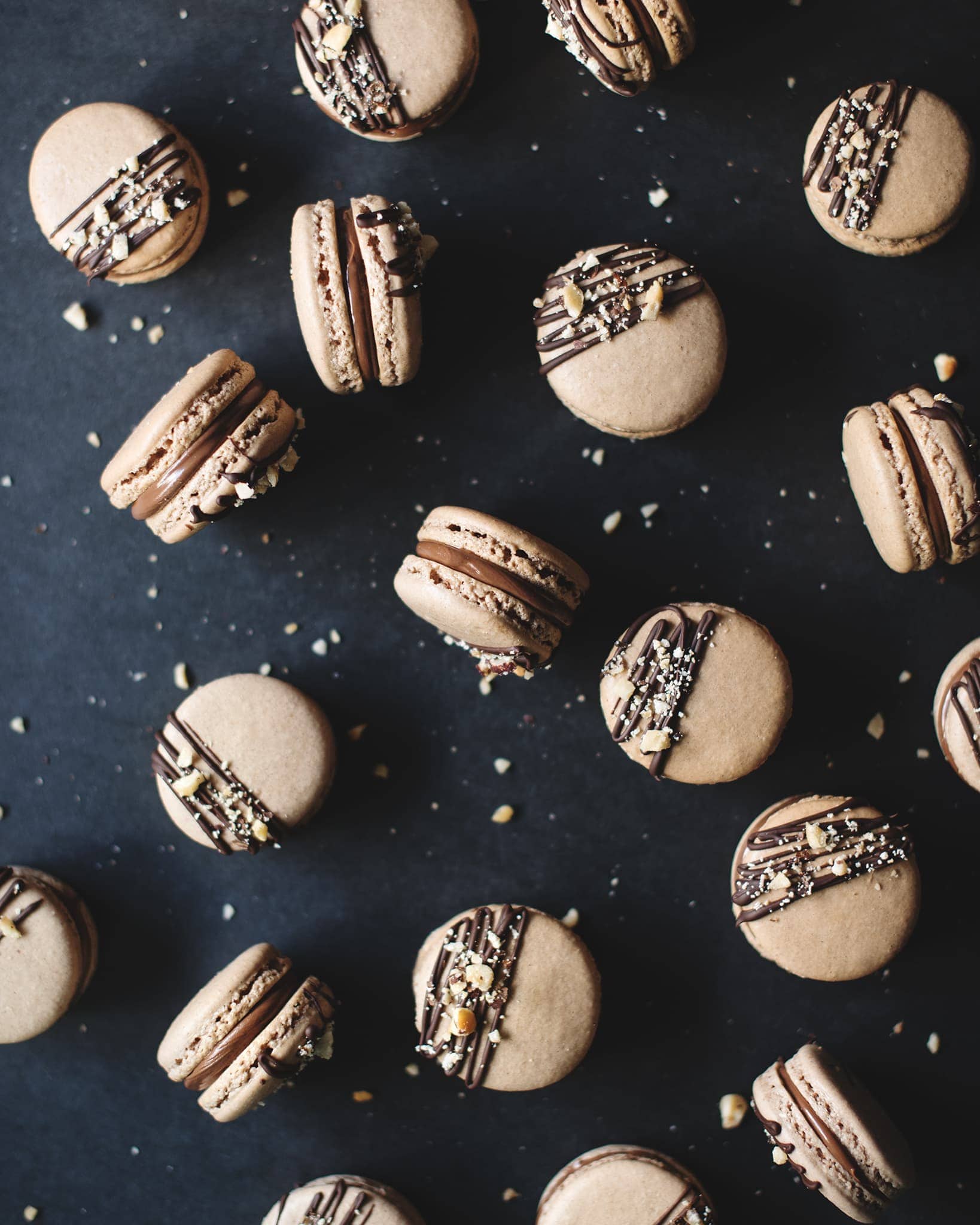 Ferrero Rocher macarons topped with dark chocolate drizzle and crushed hazelnuts scattered on a black background