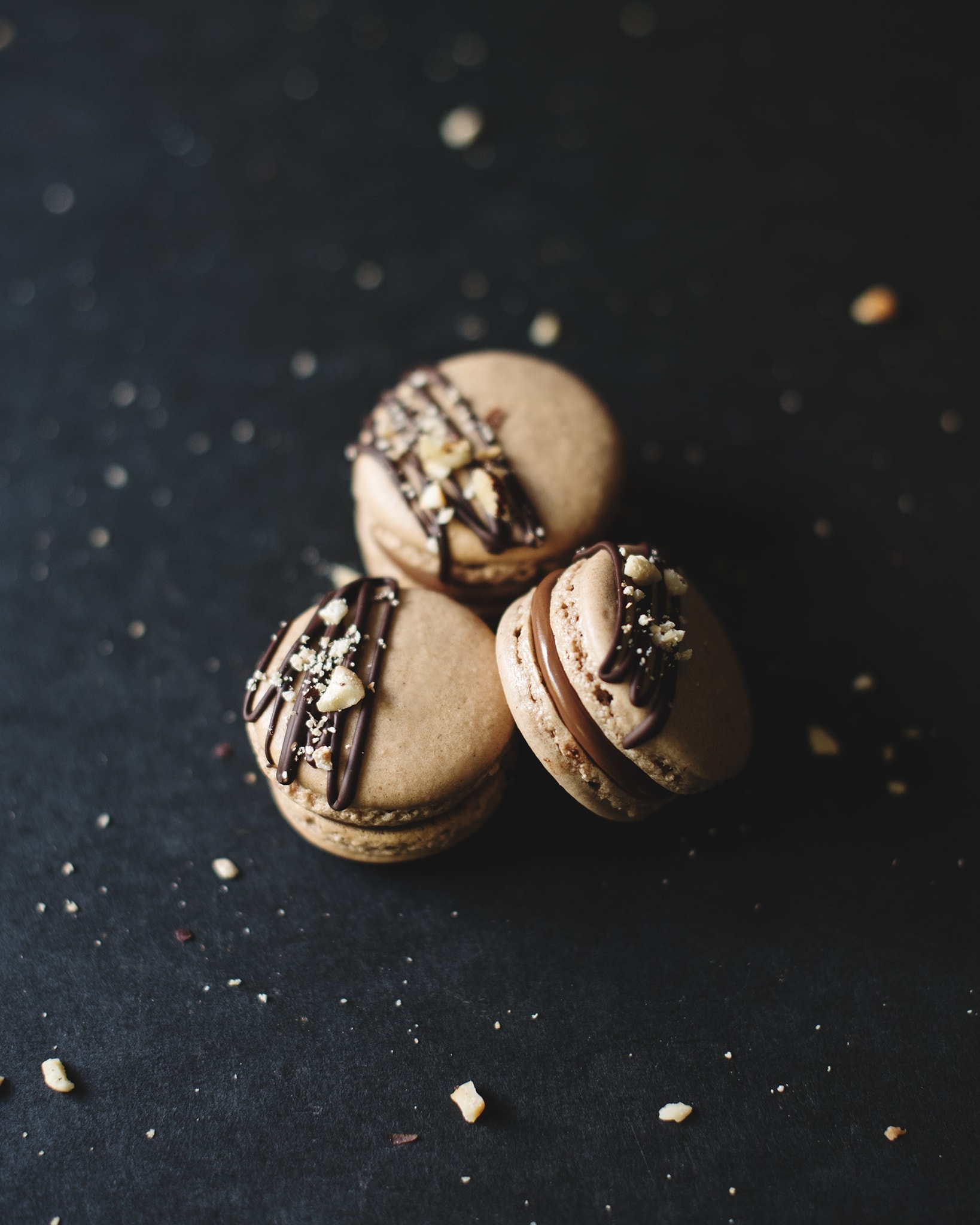 3 Ferrero Rocher macarons on a black background surrounded by crushed hazelnuts