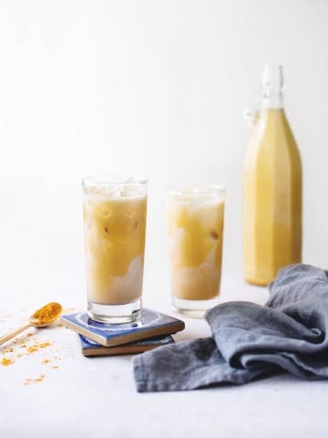 Glasses of iced golden turmeric lattes on blue coaster with blue linen napkin
