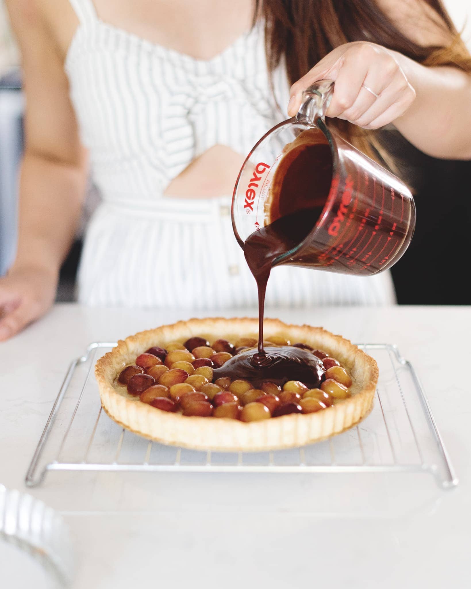 Pouring chocolate ganache on top of cherries in tart base