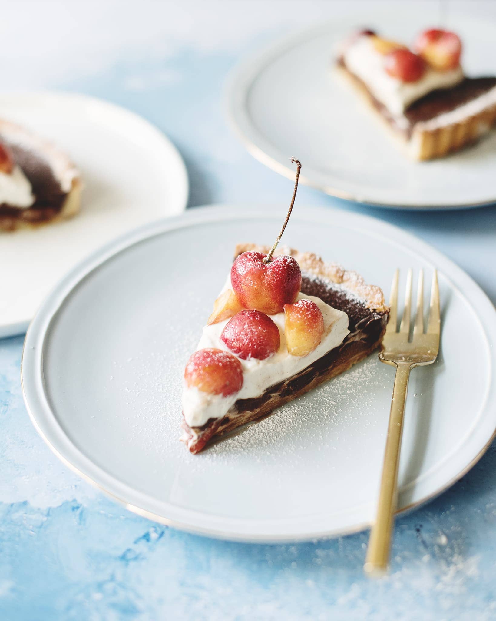 Slices of chocolate cherry tart with cardamom cream on blue plates and on blue background