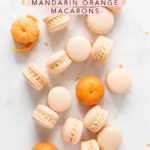 Mandarin orange macarons and mandarin oranges scattered on marble counter