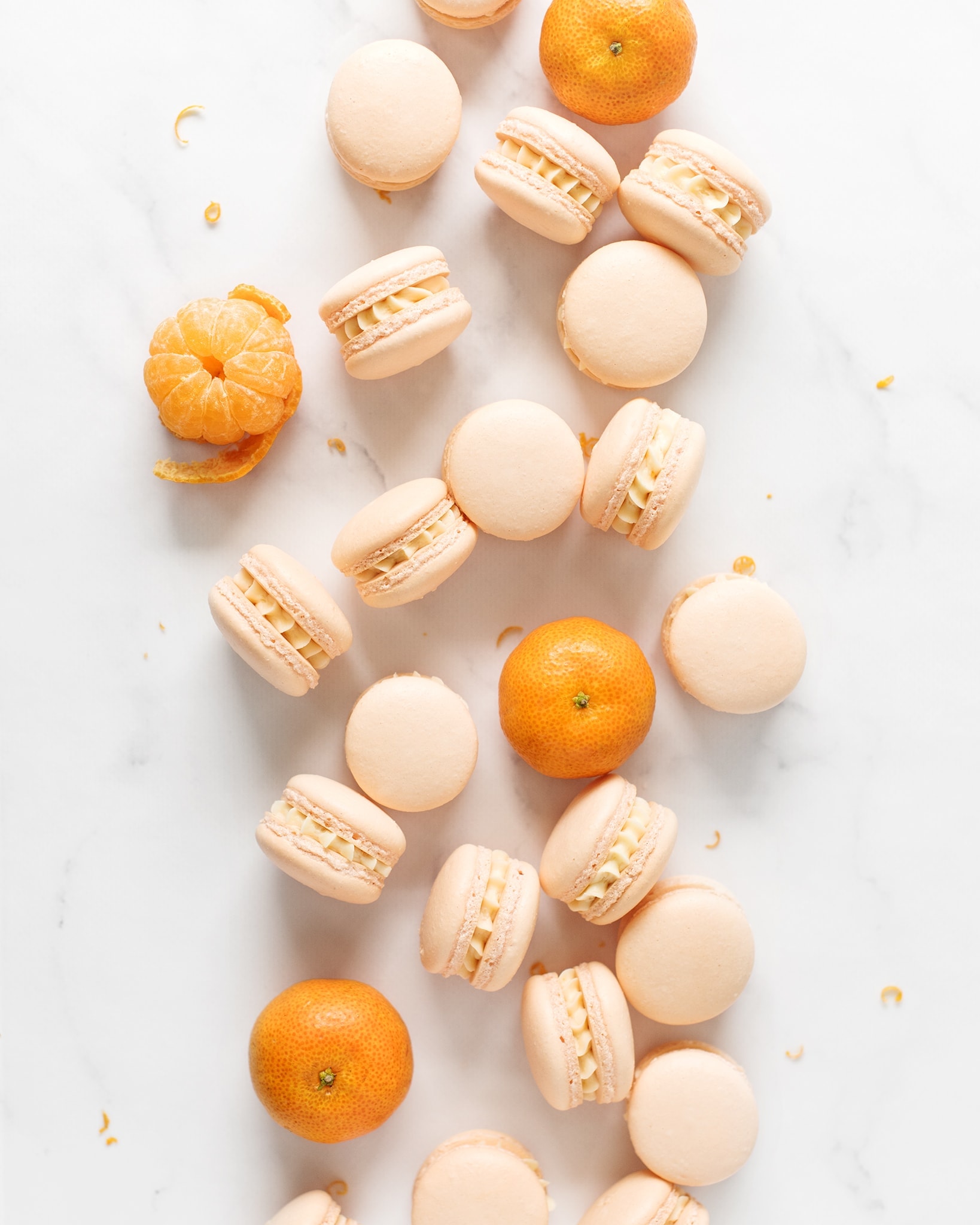 Mandarin orange macarons and mandarin oranges scattered on marble counter