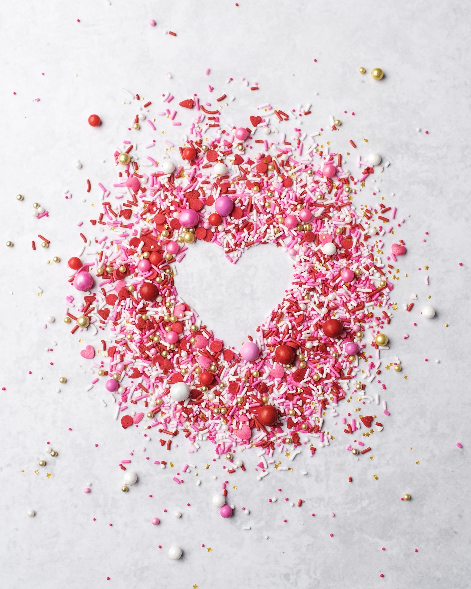Pink, red, gold, and white sprinkles surrounding a negative space of a heart shape
