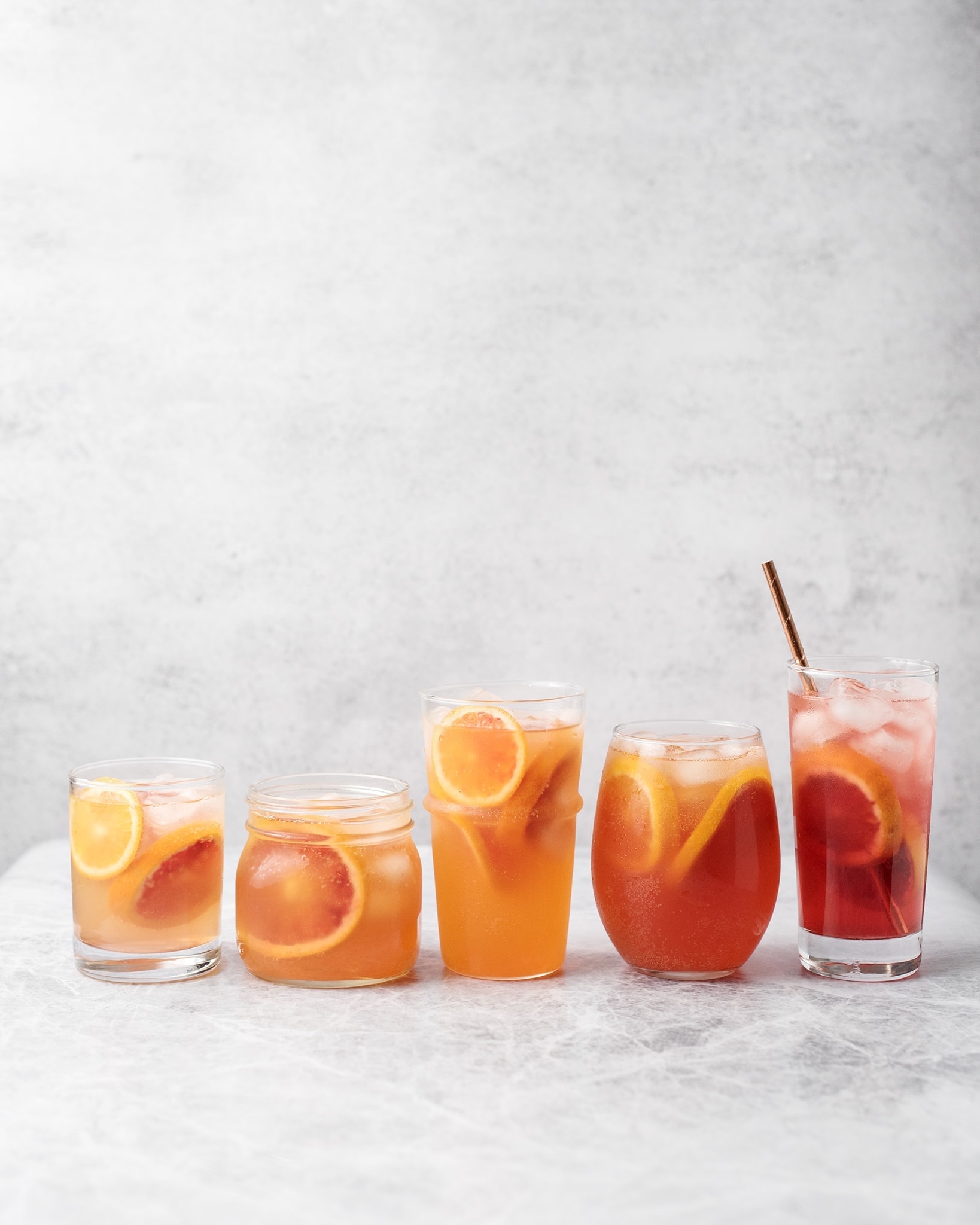 Glasses of blood orange palomas lined up as a gradient on a grey background