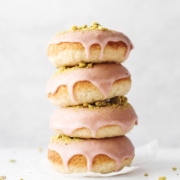 Stack of four raspberry pistachio donuts dripping with glaze