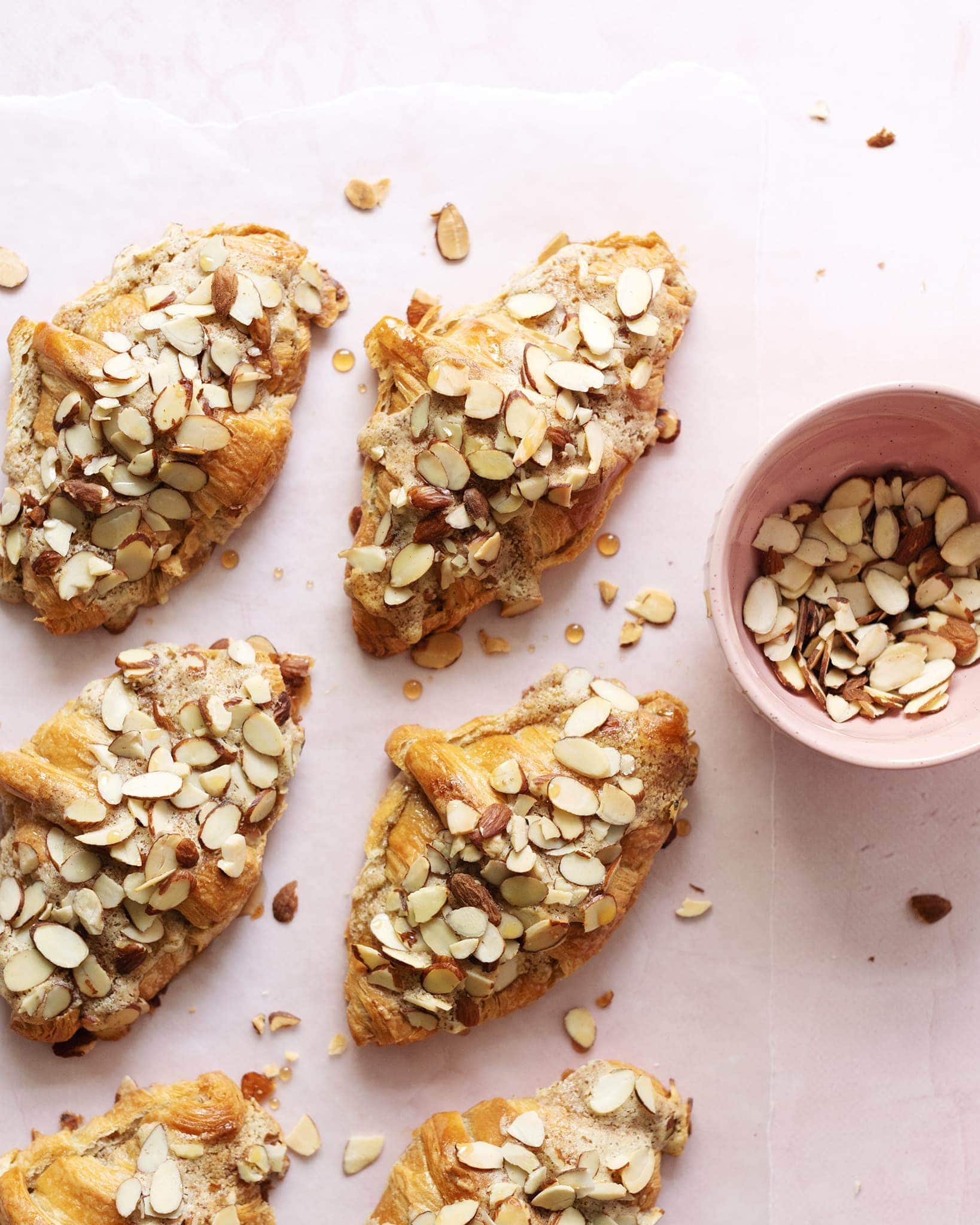 Overhead view of almond croissants sprinkled with sliced almonds on pink background