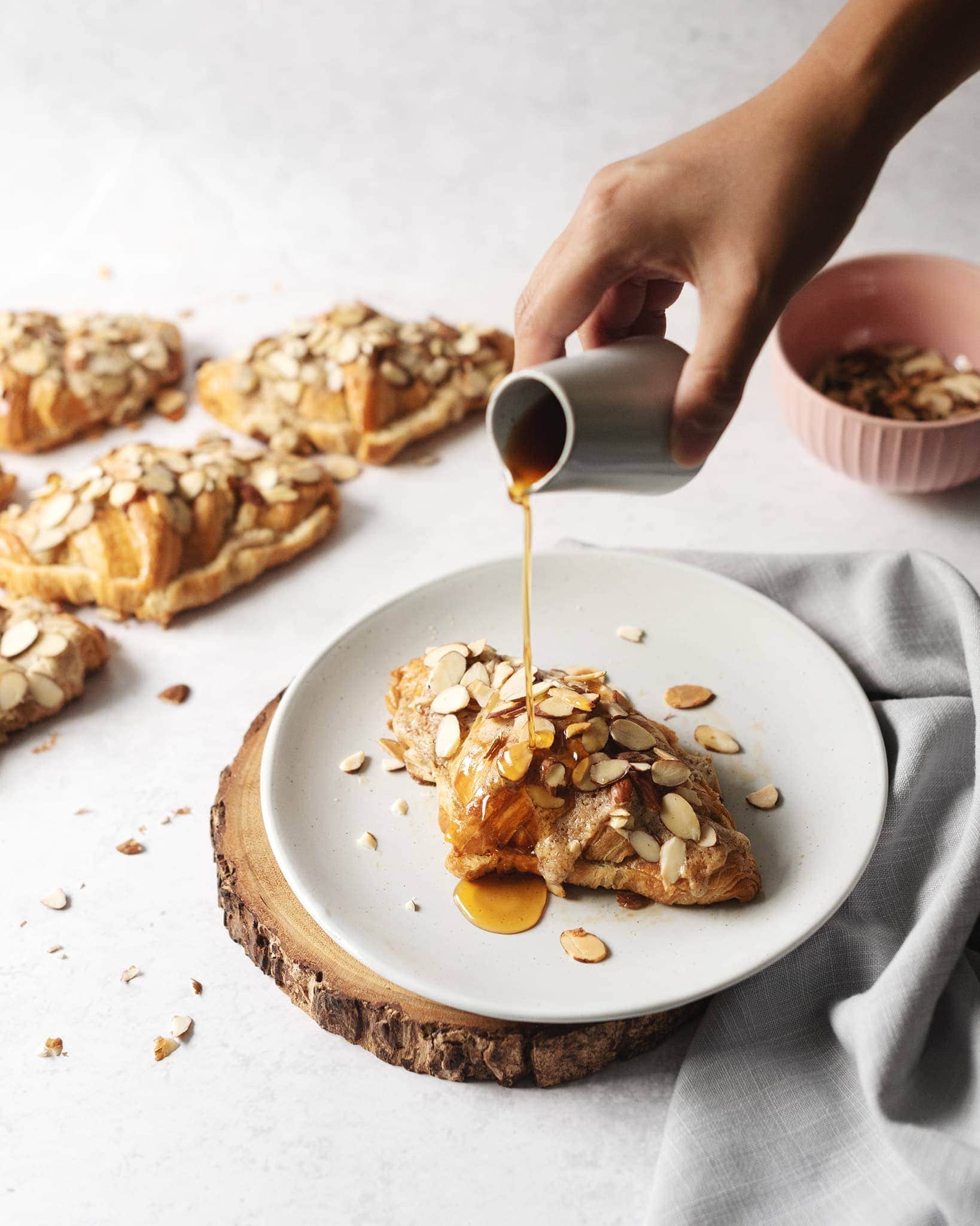 Hand pouring earl grey simple syrup on top of an almond croissant on a plate