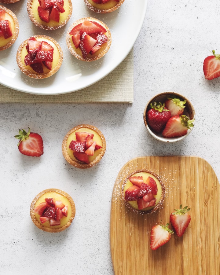 Overhead shot of strawberry lemon curd tartlets on wooden board and plate