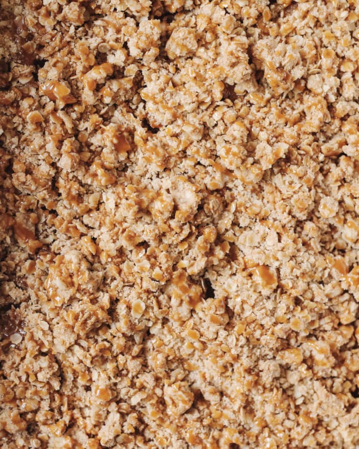 The oat crumble topping of an apple crisp drizzled with caramel sauce