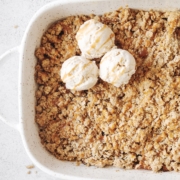 Baking dish of apple crisp topped with scoops of ice cream