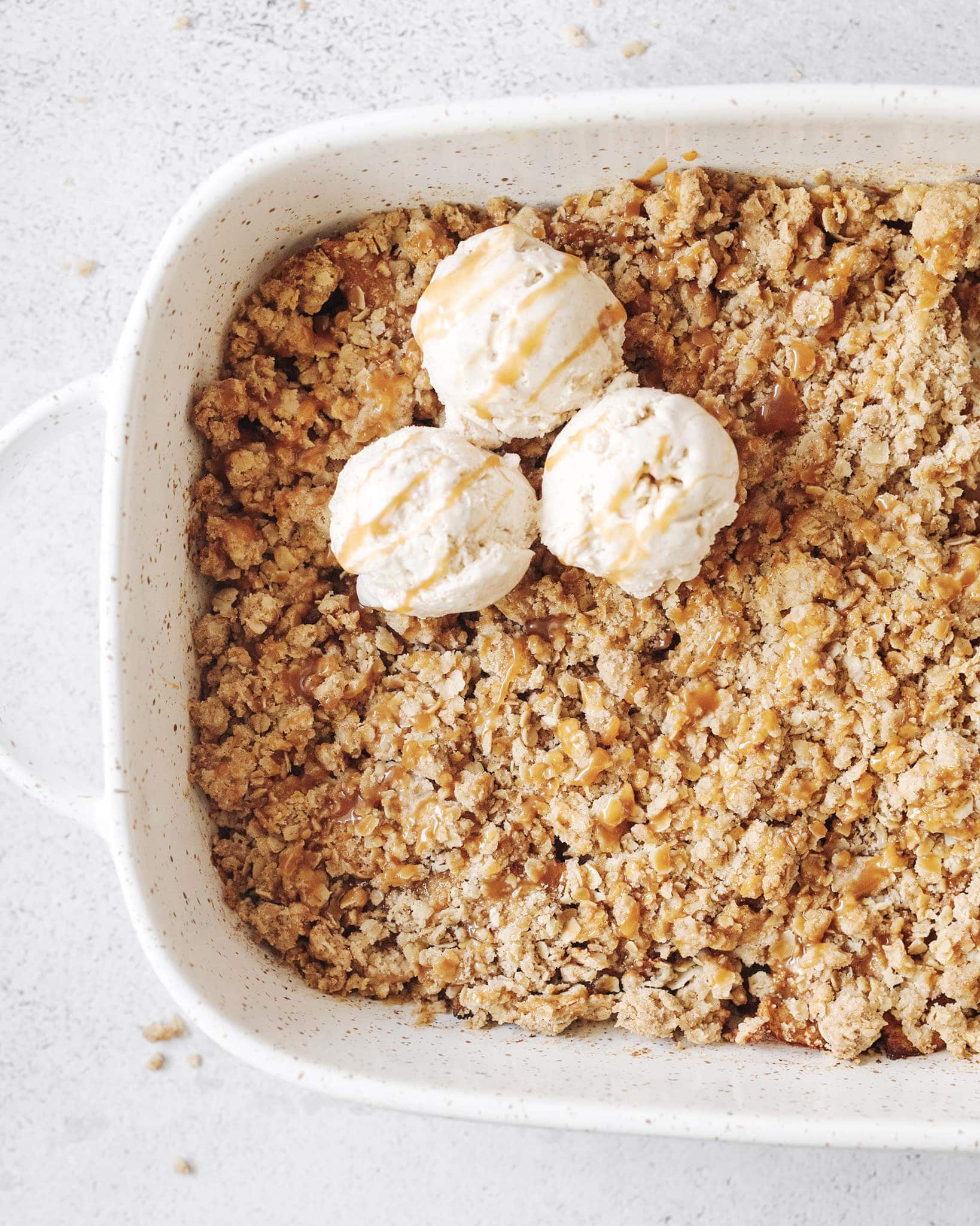 Baking dish of apple crisp topped with scoops of ice cream