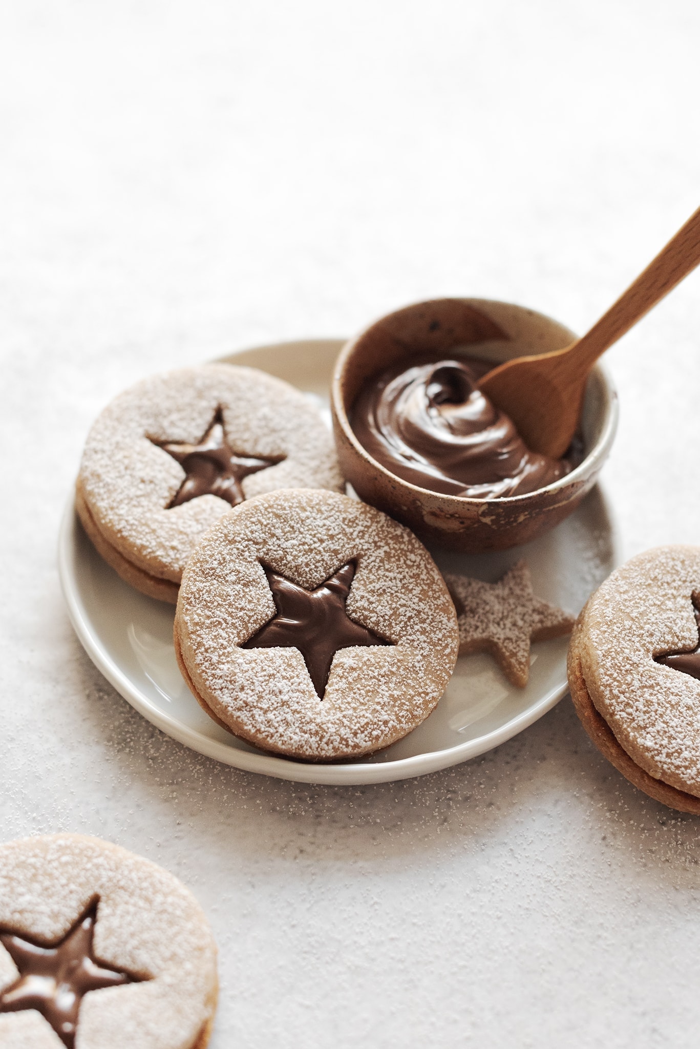 Hazelnut linzer cookies on plate with bowl of Nutella