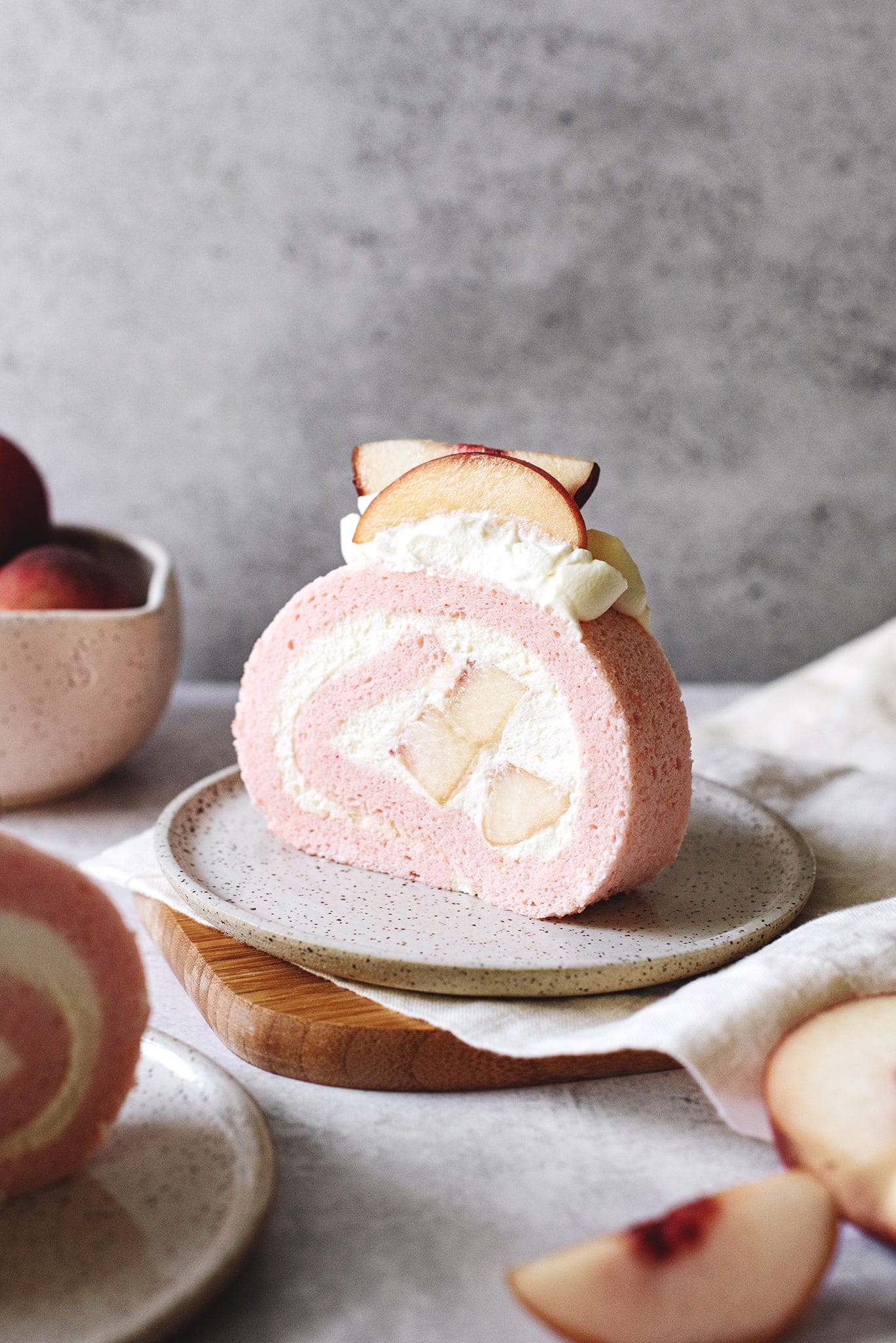 Slice of white peach swiss roll cake with fresh peaches in the middle
