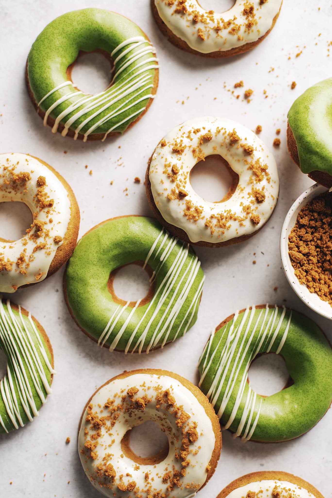 Matcha and white chocolate biscoff mochi donuts scattered on table.