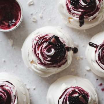 Blackberry pavlovas topped with swirls of whipped cream and blackberry sauce