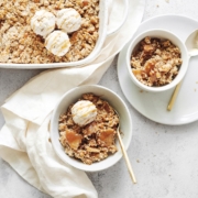 A baking dish and bowls of caramel apple crisp topped with ice cream
