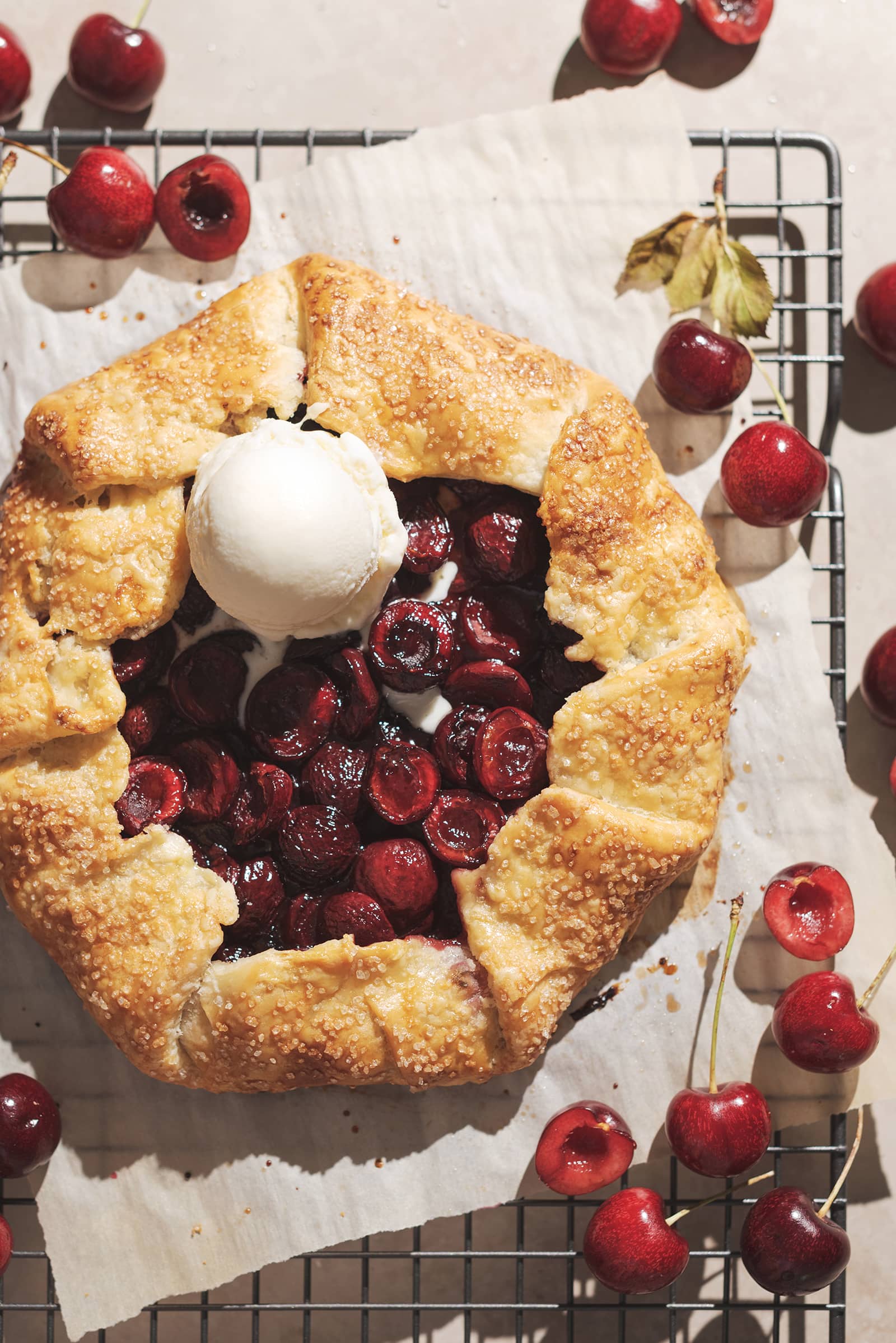 Cherry galette with a scoop of vanilla ice cream on top of it on a metal rack.