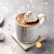 A cup of earl grey hot chocolate topped with a marshmallow and fairy lights in the background