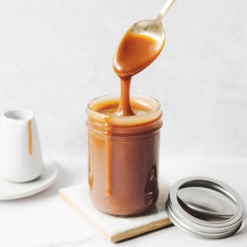 Spoon dripping with caramel sauce above glass jar