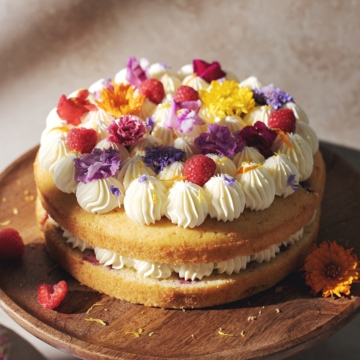 Lemon raspberry cake with layers of lemon buttercream and fresh flowers on top.