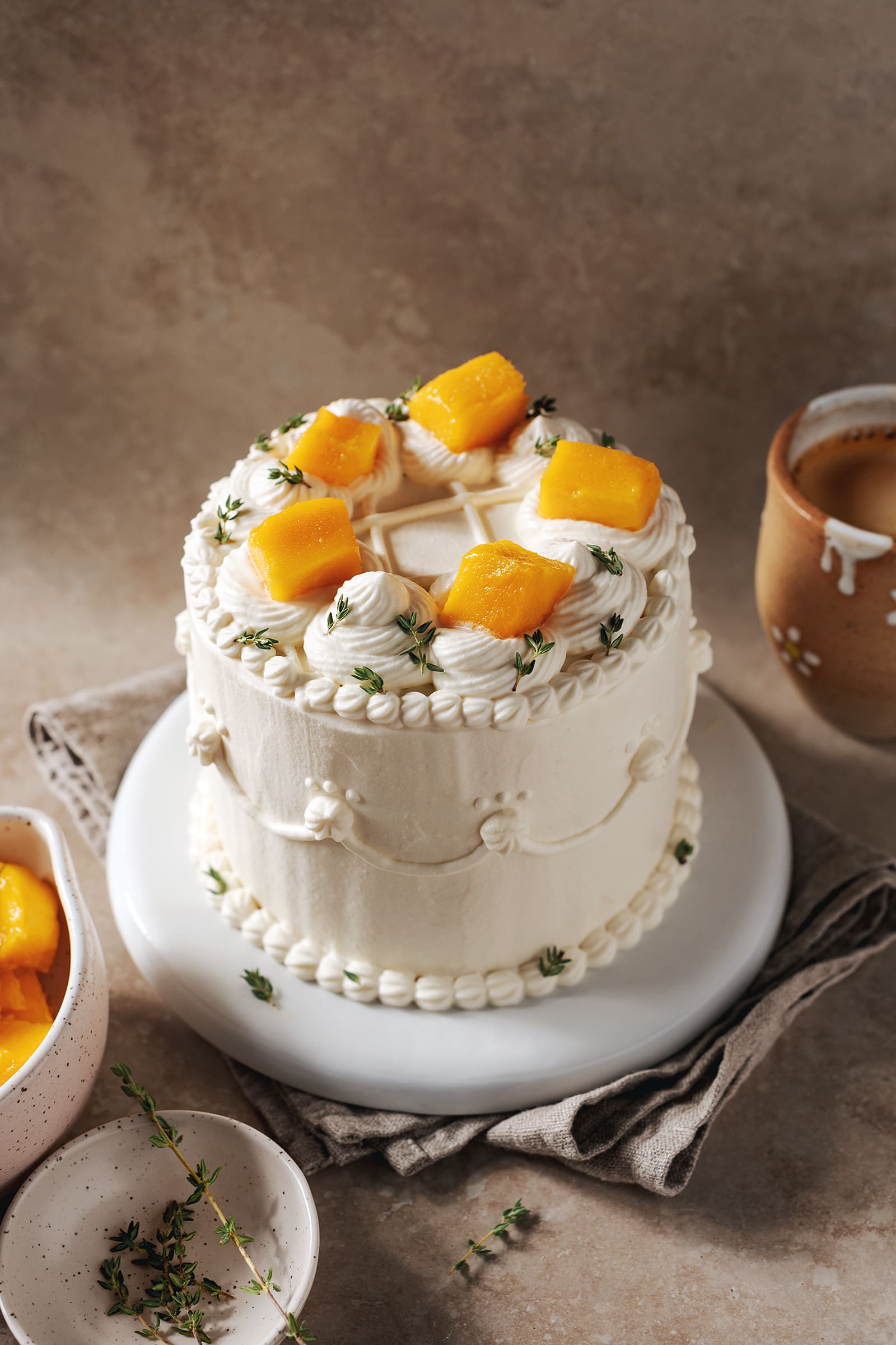 Cake covered with whipped cream and topped with mango chunks sits on a white plate.