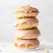 Stack of four raspberry pistachio donuts dripping with glaze