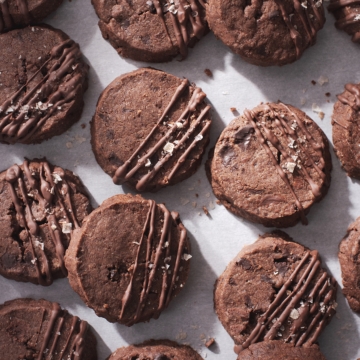 Many chocolate sablé cookies on scattered on baking sheet