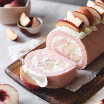 A slice of white peach swiss roll cake cut from the roll