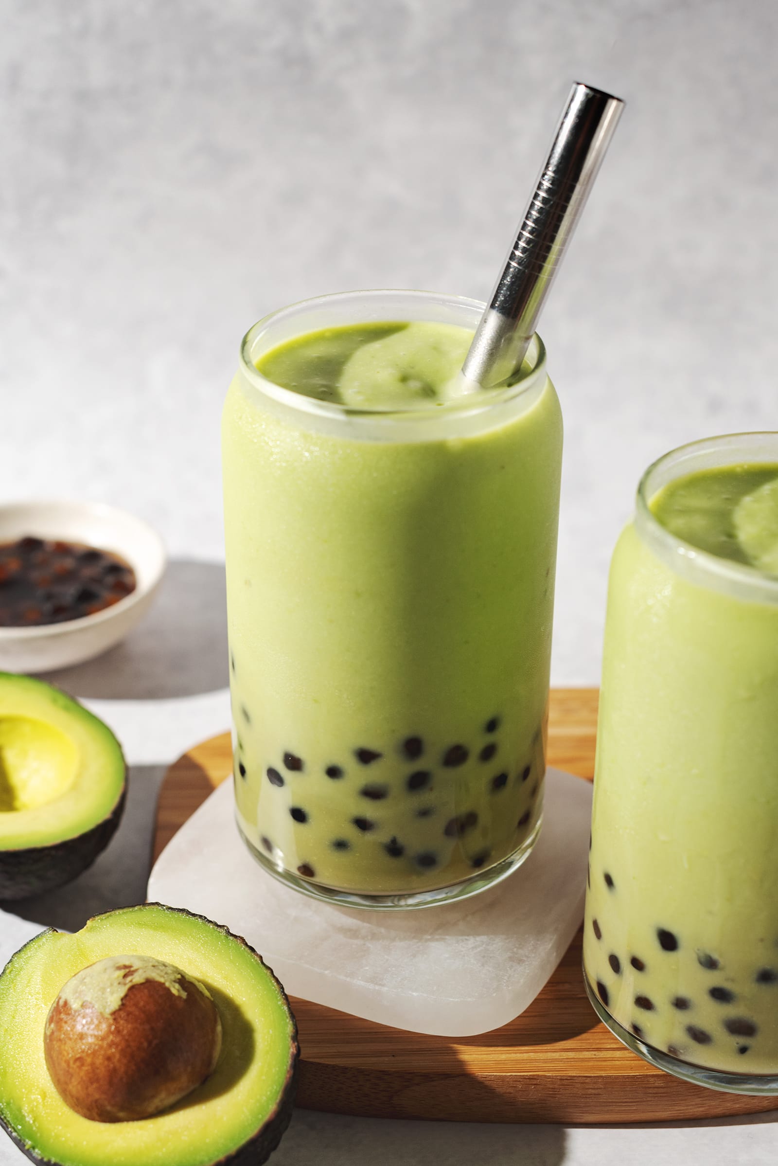Glass of avocado boba with a metal straw on a coaster.