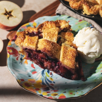 A slice of blueberry apple pie on a plate with a scoop of vanilla ice cream.