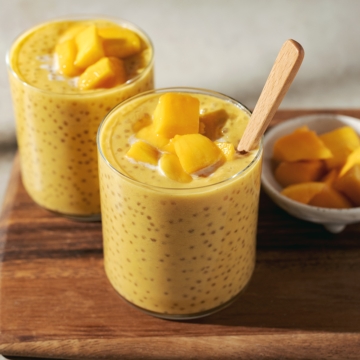 Two glasses of mango sago topped with mango chunks on a wooden platter.