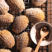 Pumpkin madeleines scattered on a wire rack with a small bowl of pumpkin pie spice.