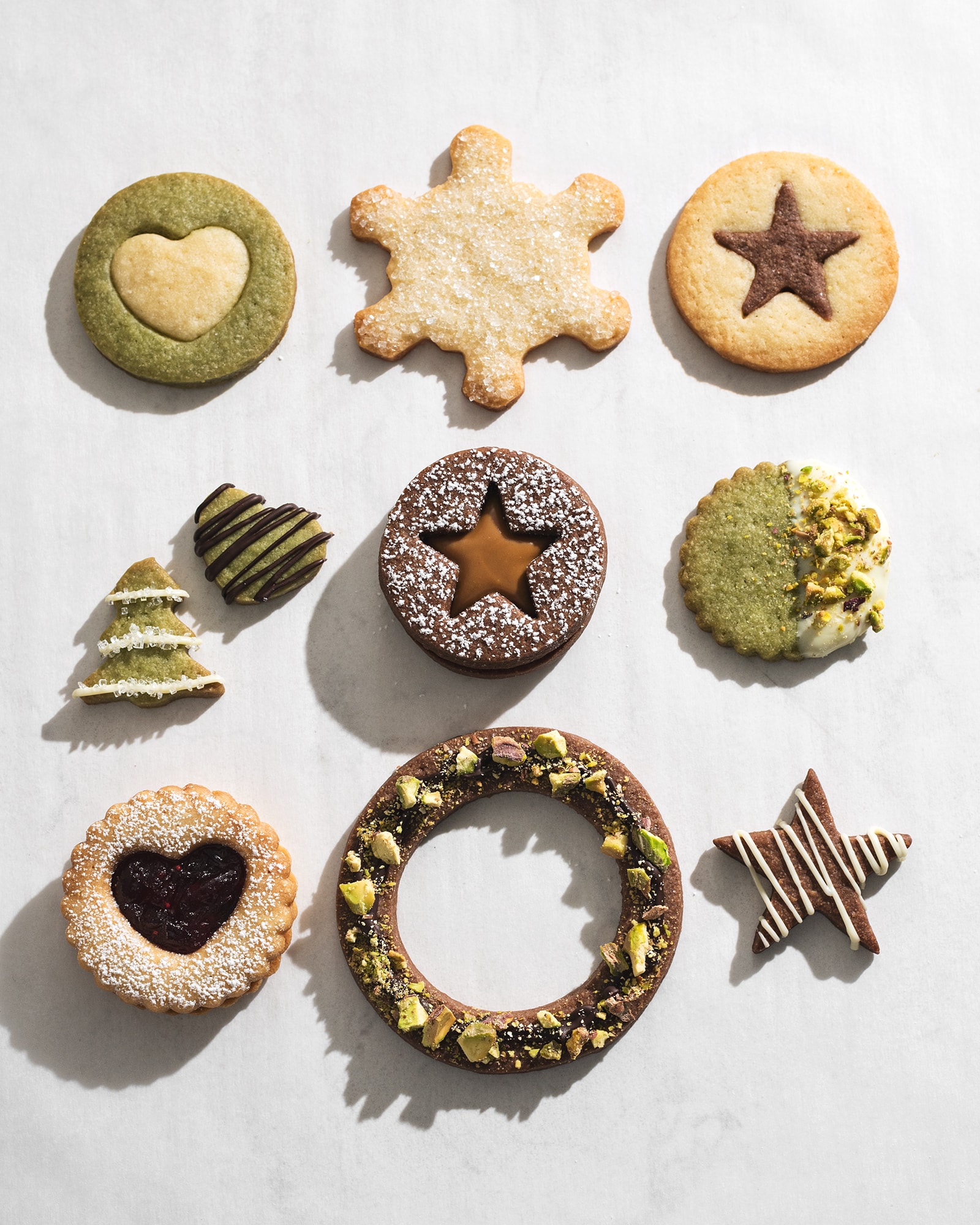 10 different decorated butter cookies with star and heart cutouts, chocolate drizzles, and pistachios.