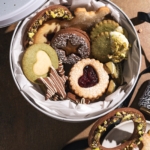 Assorted butter cookies in a round tin with cookies scattered around it.