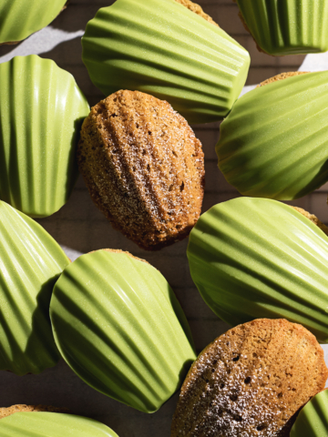 Matcha madeleines on parchment paper, some plain and some with a matcha chocolate shell.