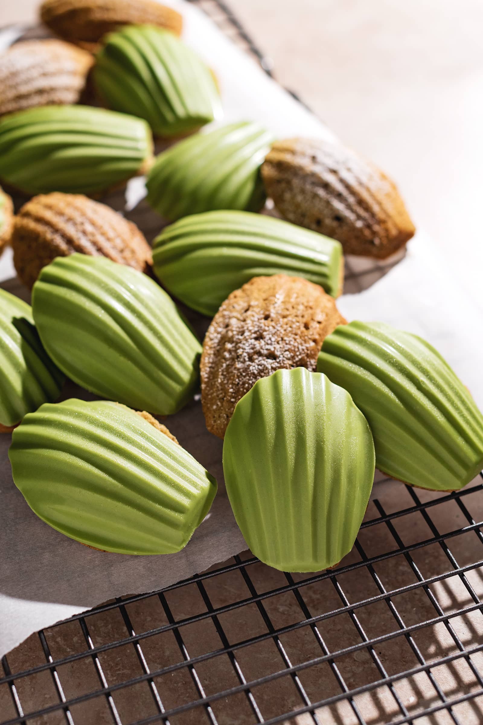 Madeleines covered with a matcha white chocolate shell on a wire rack.