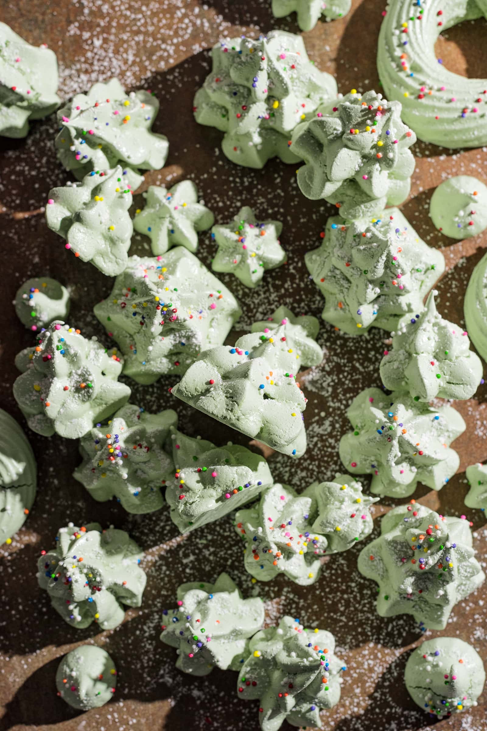 Green meringues shaped like christmas trees scattered on a wooden board.