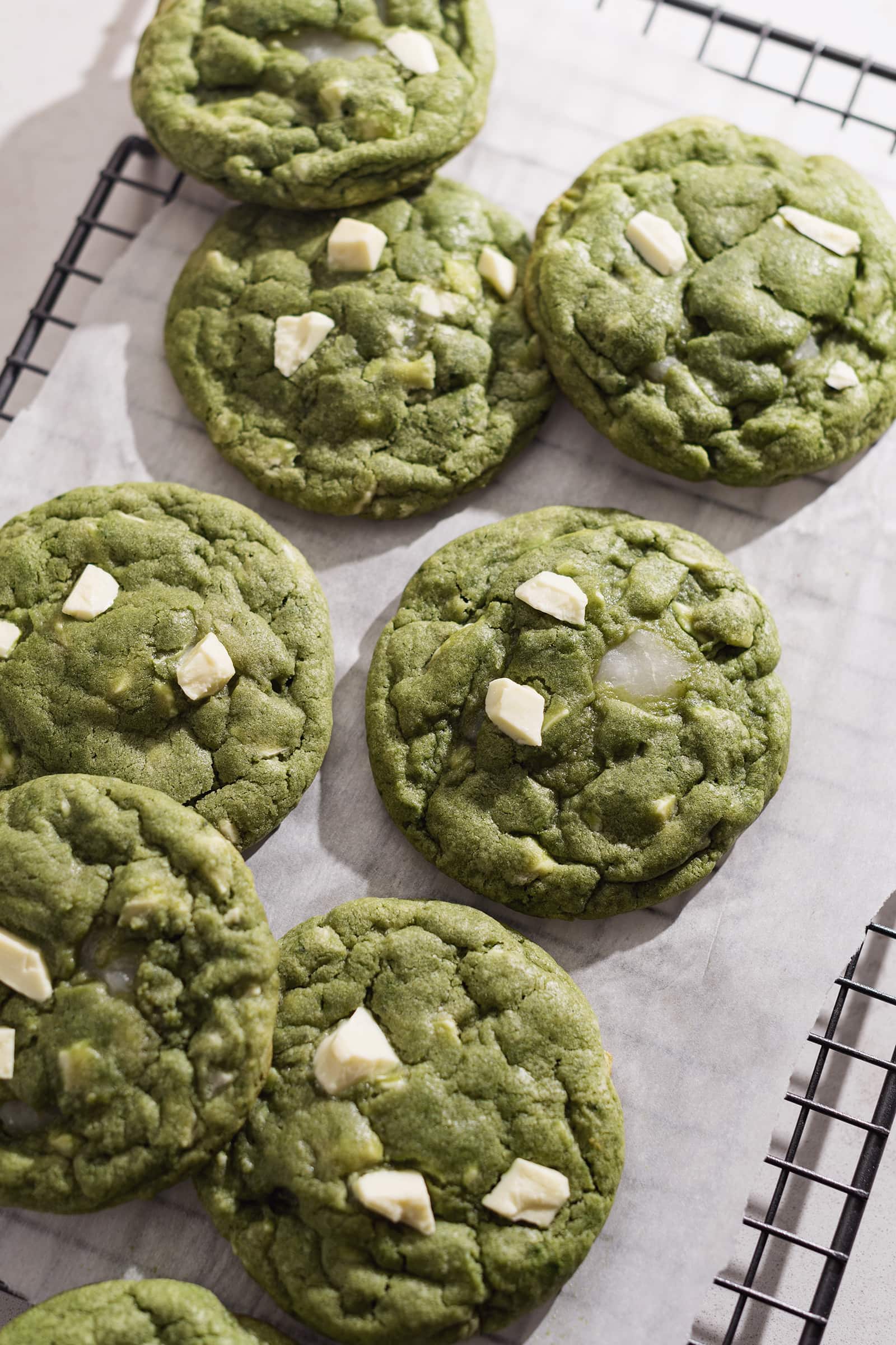 Matcha mochi cookies scattered on top of a wire rack and parchment paper.