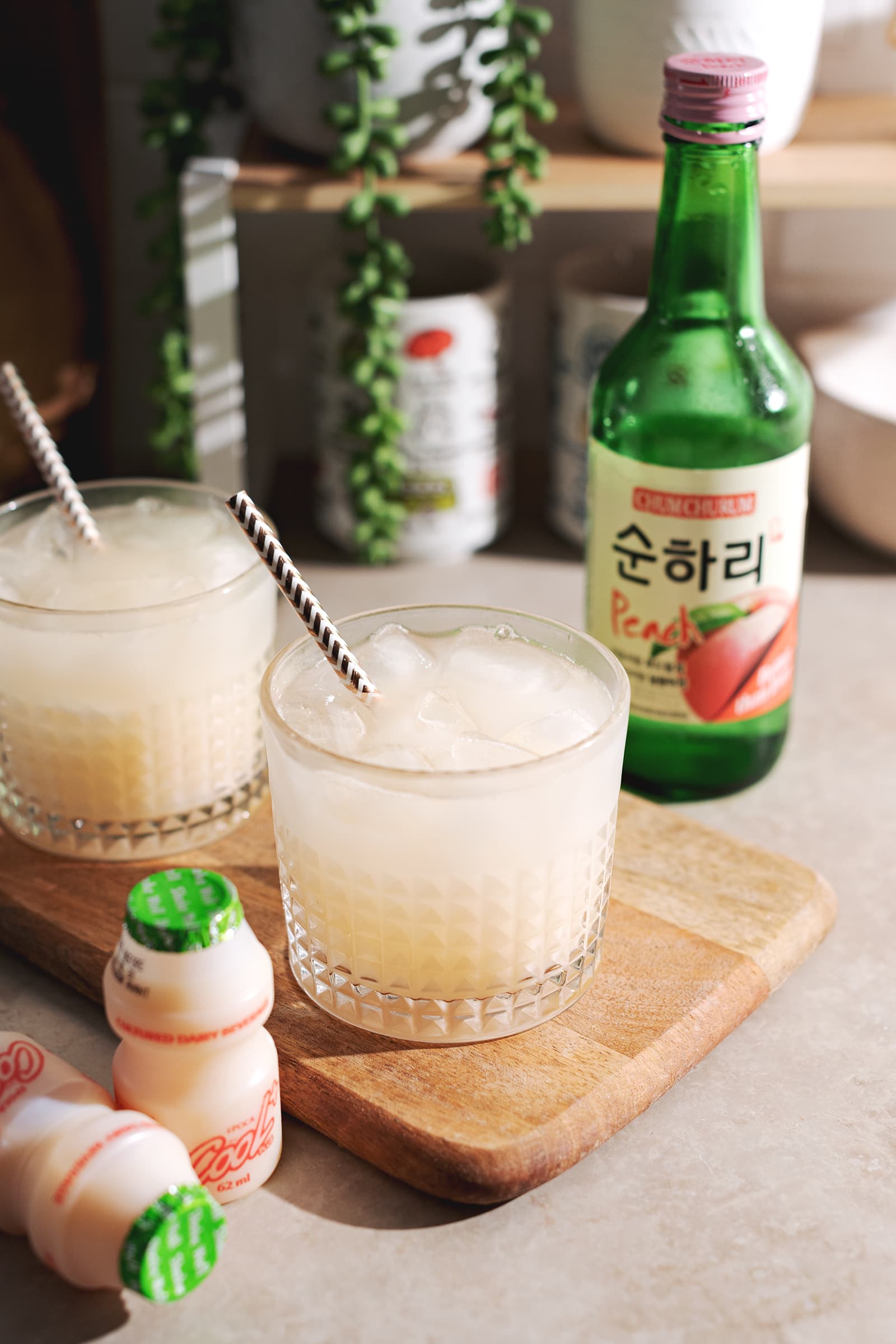 Soju yakult cocktail in a glass with soju bottle in the background and yakult in the foreground.