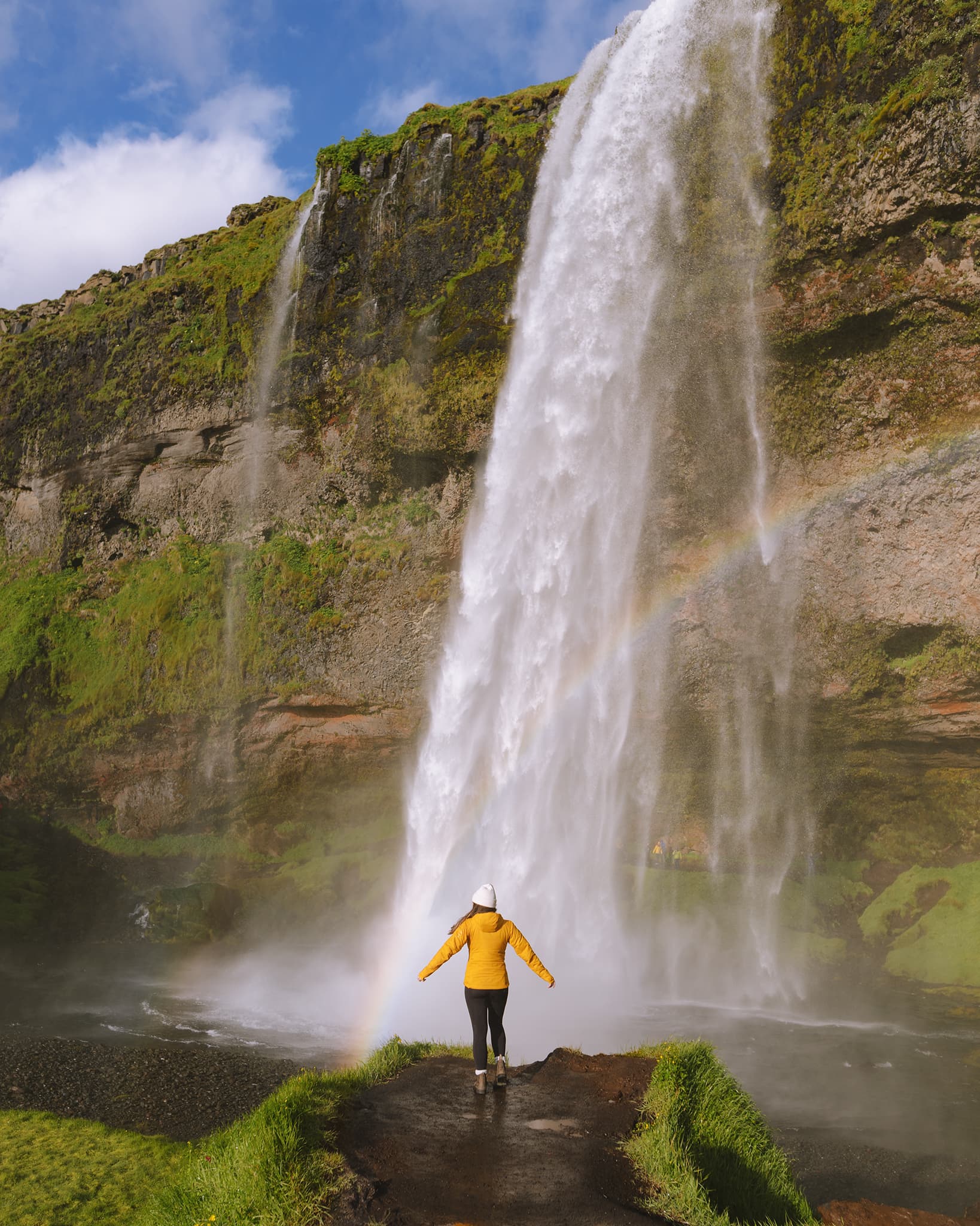 Girl in yellow jacket standing in front of a waterfall.