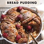 Croissant bread pudding in a baking dish with two spoons where a slice was cut out from it.
