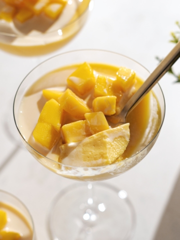A spoonful of mango pudding resting in the glass with mango chunks on top.