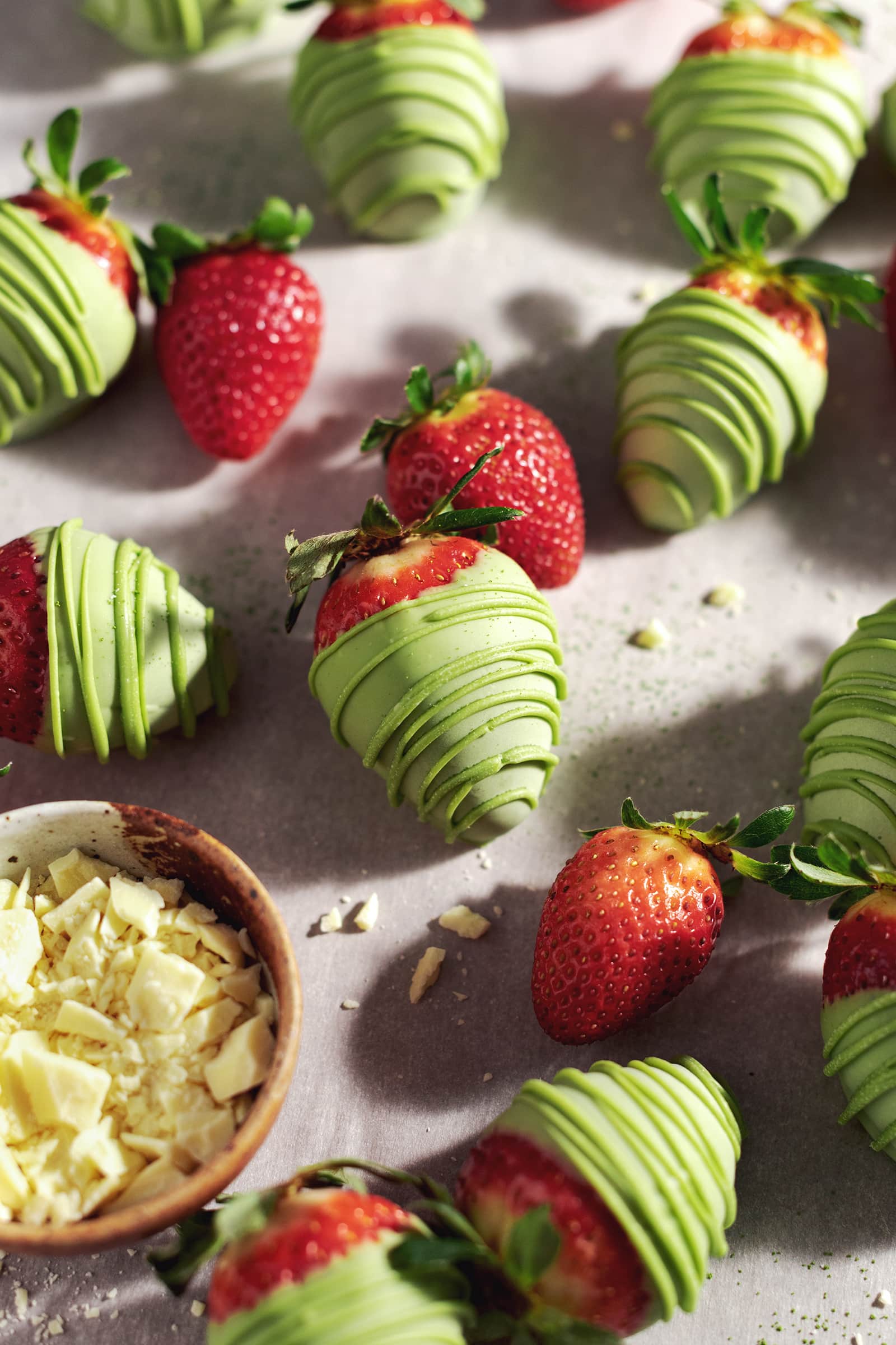 Strawberries dipped in green matcha white chocolate scattered on table with fresh strawberries.