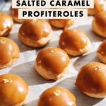 Profiteroles covered with salted caramel and gold flakes lined up parchment paper.