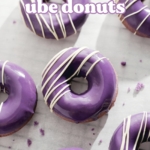 Purple ube donuts with white chocolate drizzles scattered on parchment paper.