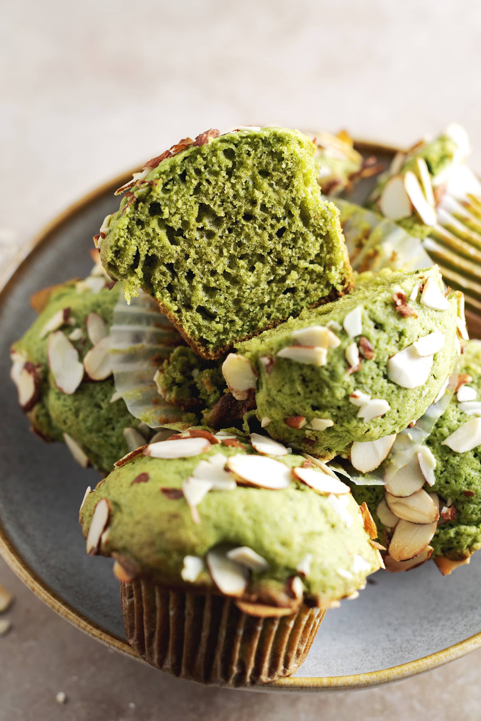 A matcha muffin cut in half to show texture sitting on top of pile of muffins.