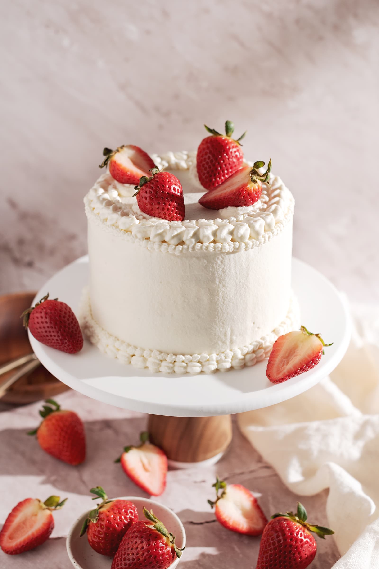 Cake covered in whipped cream and strawberries on a cake stand.