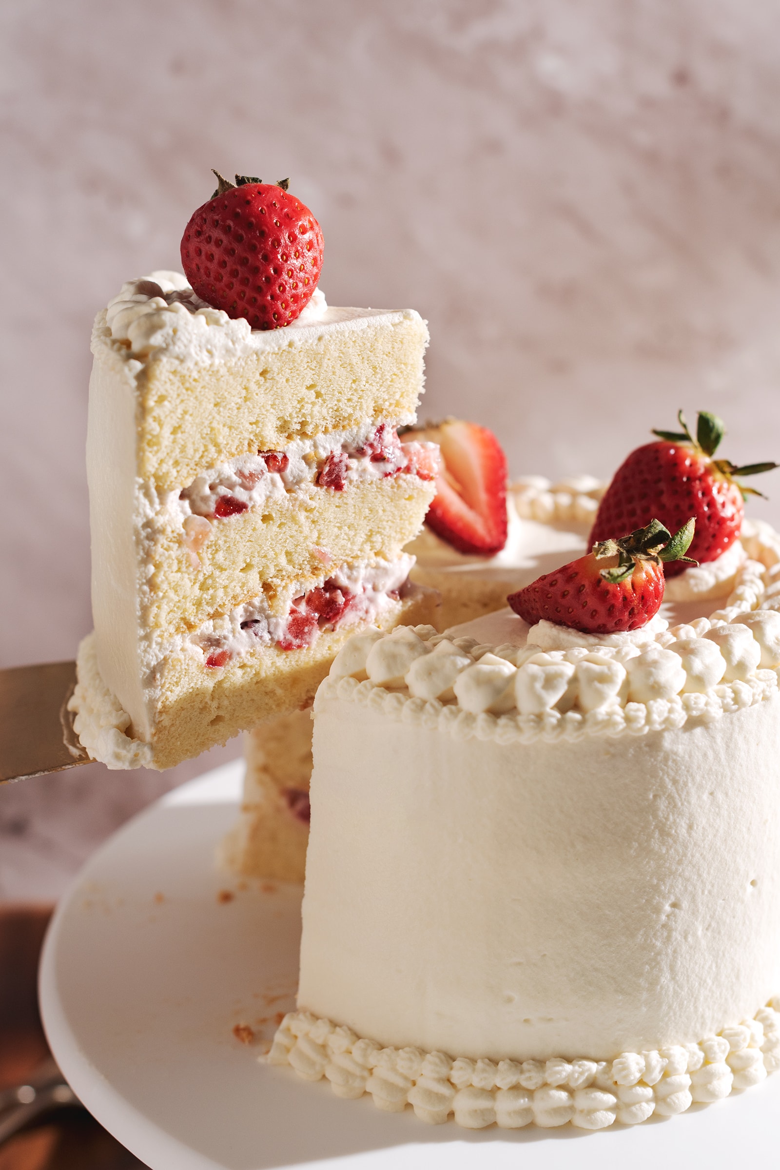 A slice of strawberry chiffon cake lifted above the rest of the cake with a cake server.