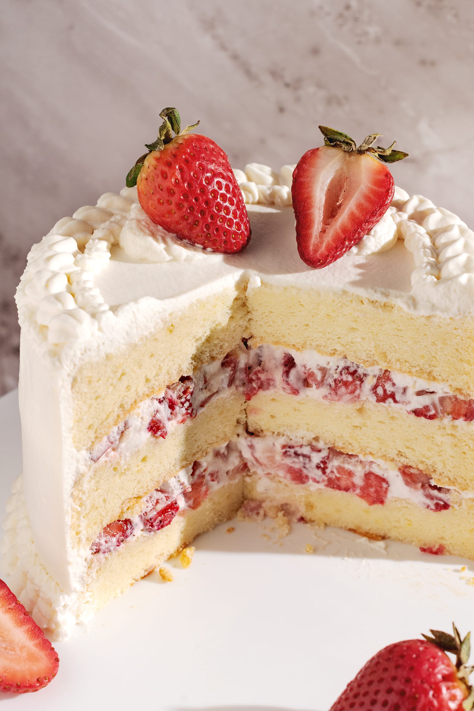 Cross-section of cake showing layers of chiffon cake, whipped cream, and strawberries inside.